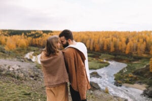 a couple close together in nature with autumnal trees in the background