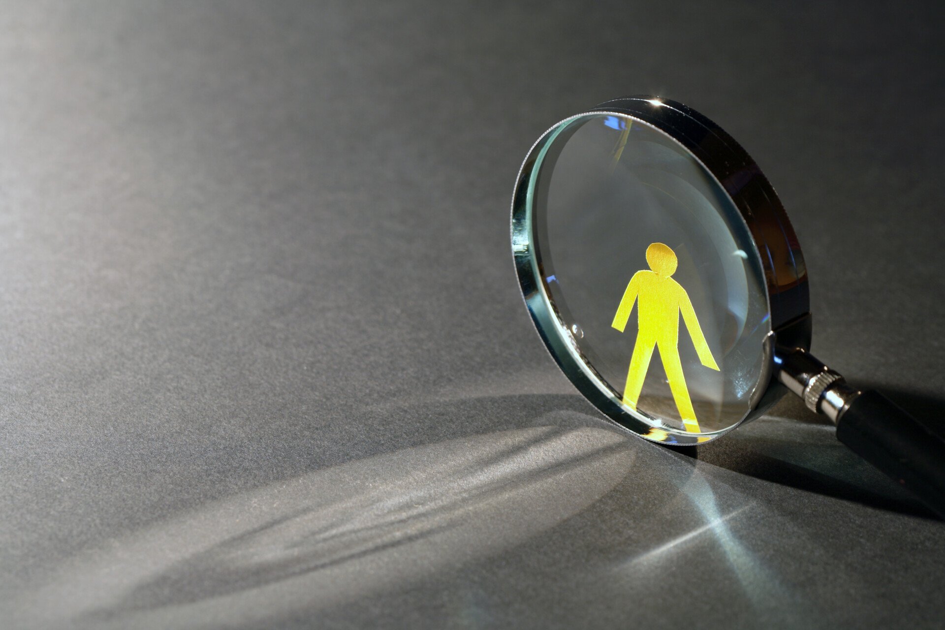 Yellow paper man near magnifying glass on dark background with beam of light