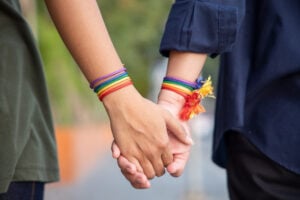 Hands of two people holding hands while wearing rainbow-coloured bracelets