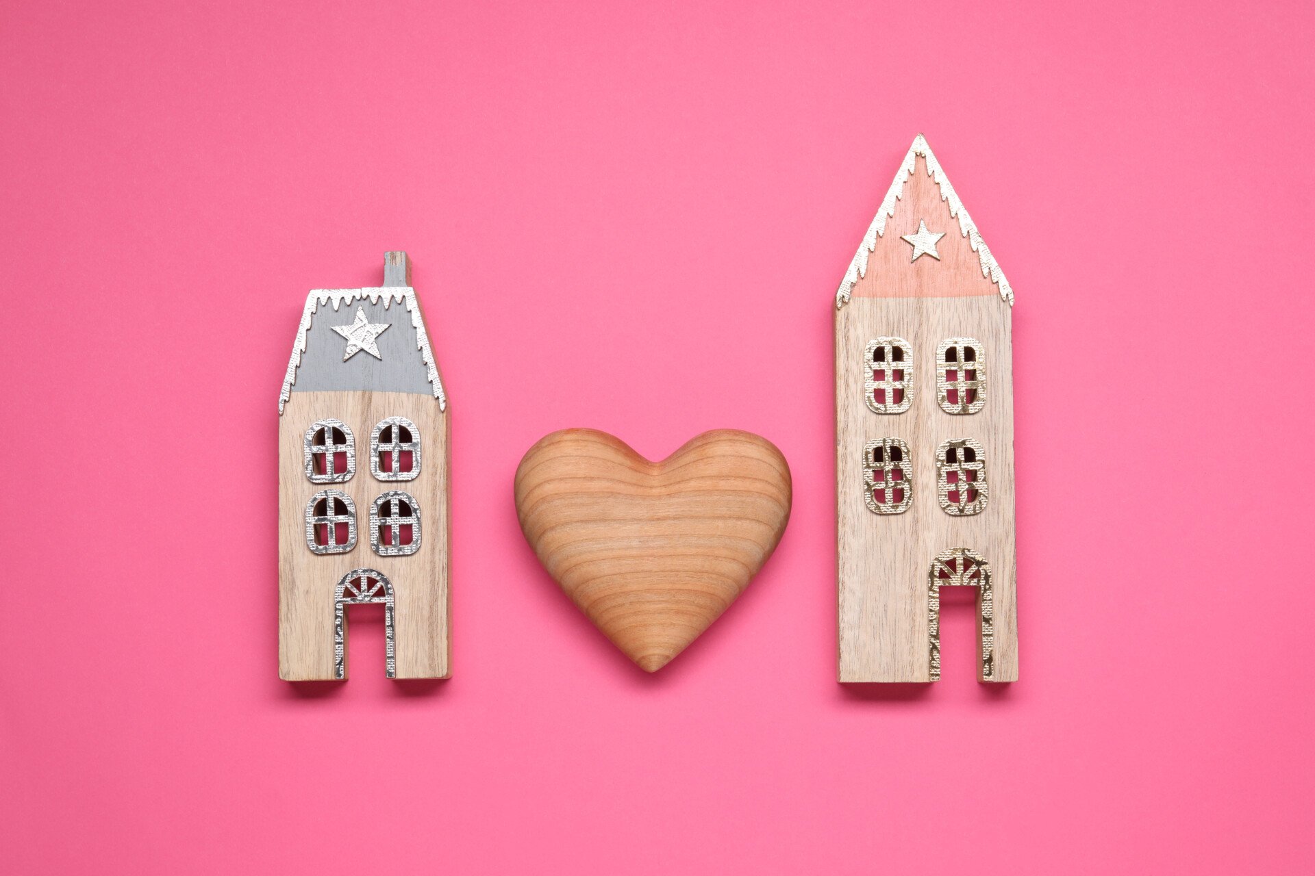 Decorative heart between two house models on pink background