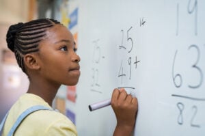 A girl solving a math question on a white board at school.