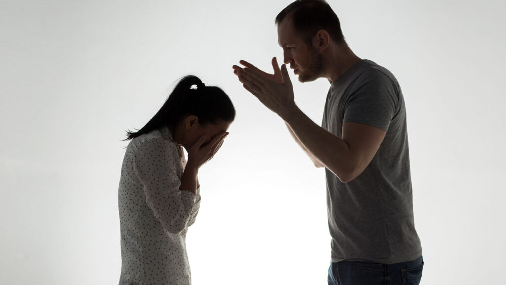 a man leaning over a woman with her head in her hands. Projecting blame onto her