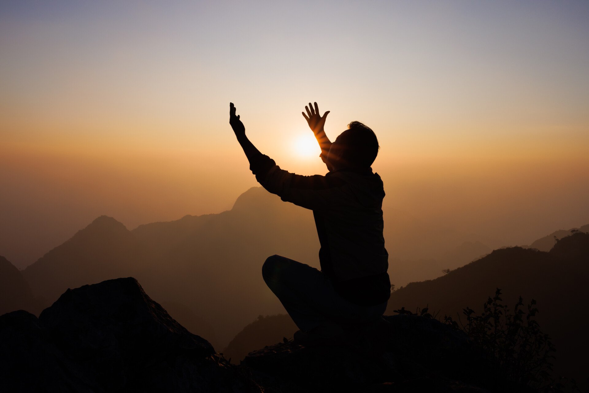 Silhouette of a man is praying on a mountain. 